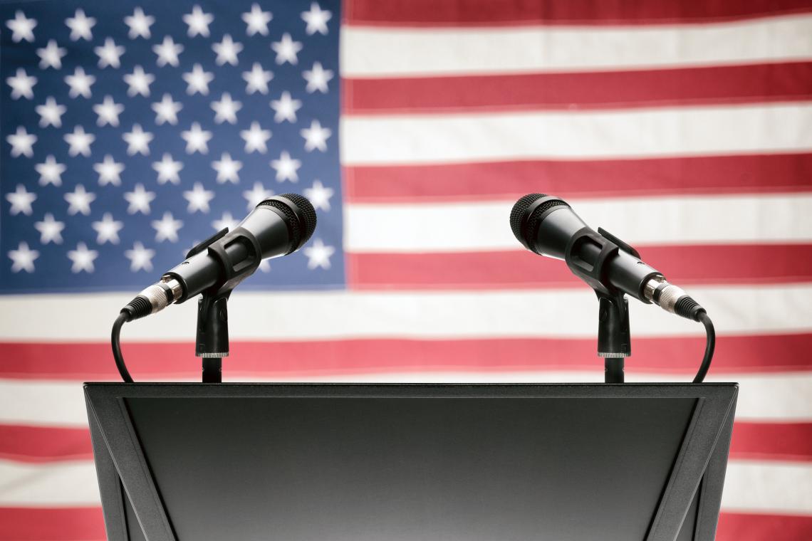 Two microphones on a podium in front of American flag